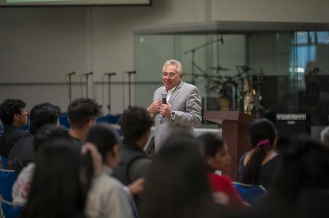 Speaker delivers engaging lecture in university hall to attentive audience with musical equipment in background.