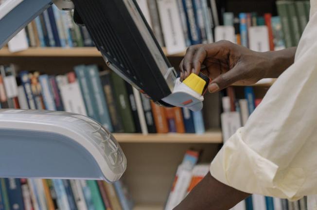 Hands scanning a textbook in a modern library, showcasing technology and learning resources.