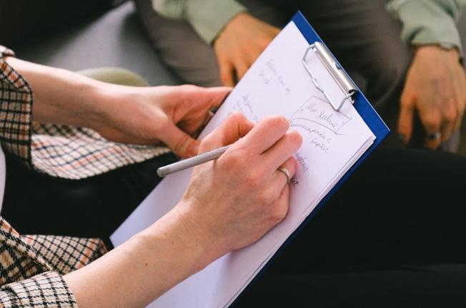 Close-up of a therapist taking notes during a session, focusing on the clipboard and pen.