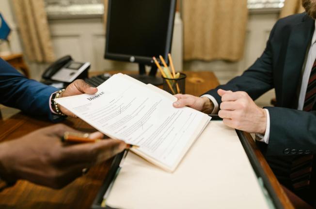Close-up of hands exchanging divorce documents during legal proceedings in office.